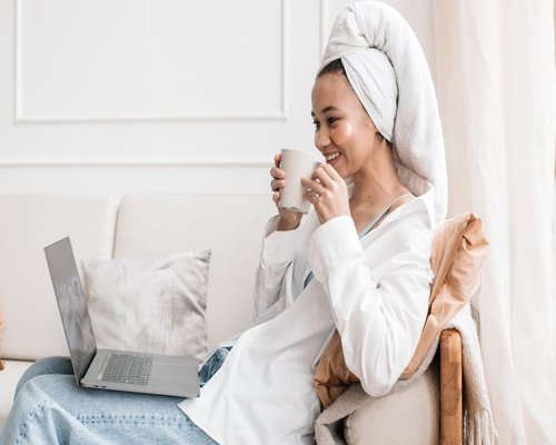 Woman drinking coffee and resting her eyes while working on a laptop in a well-lit room